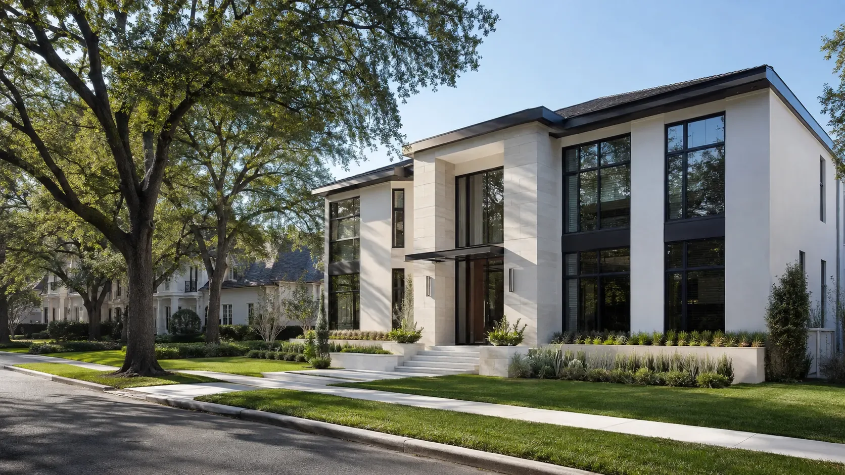 A contemporary two-story Houston house in white stucco and limestone with tall black-framed windows, seen from the street on a clear day beneath a mature live oak